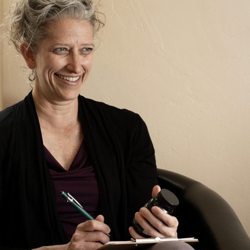 Gwen-session Gwen Diaz, AyD., in a session with a patient, while taking notes and holding a bottle of herbs in her office in Paonia, Colorado. Gwen Diaz, AyD. offers healthcare services locally, and worldwide, and specializes in perimenopause care.